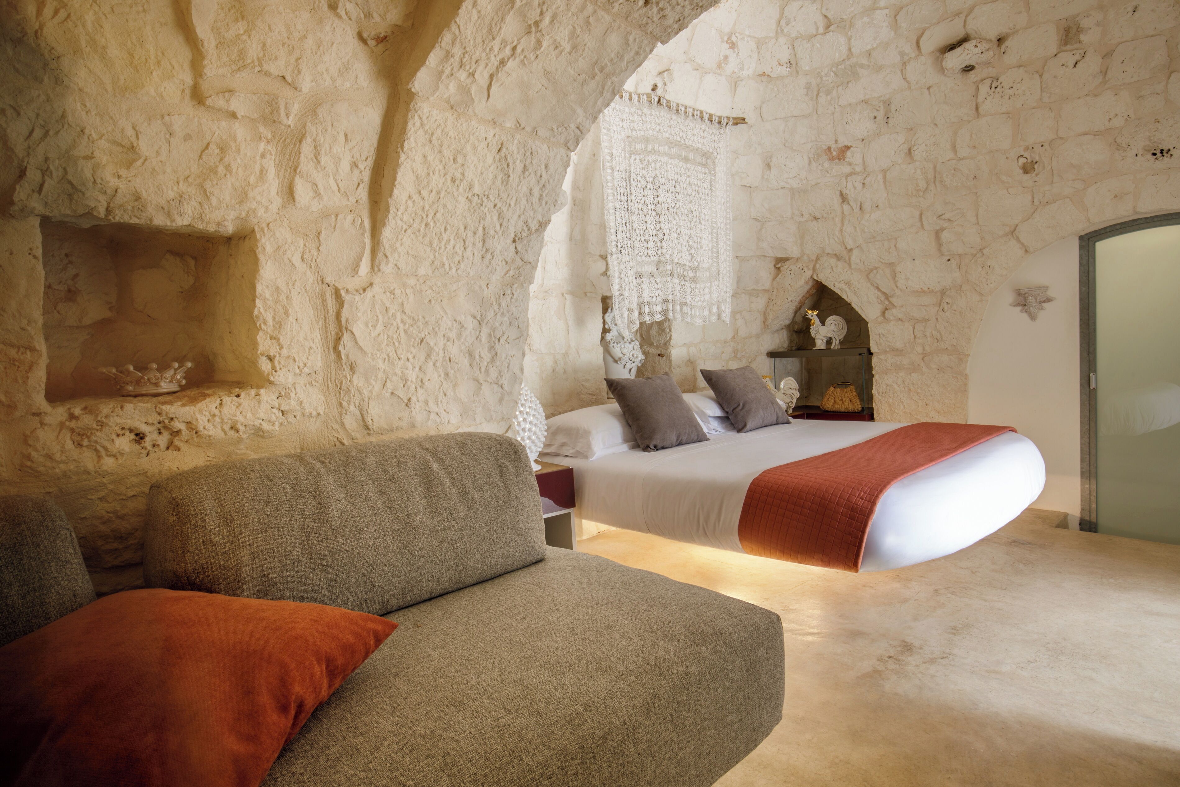 Un dormitorio con pared de piedra, una cama con almohadas, un sofá y un objeto decorativo en la pared.