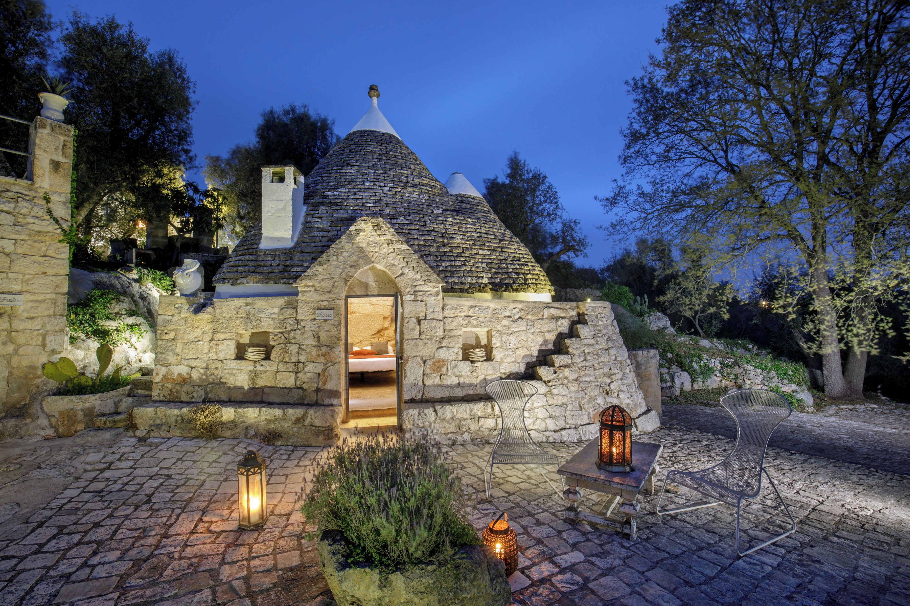 Edificio de piedra con techo cónico, una pequeña entrada arqueada y una cama visible en su interior.