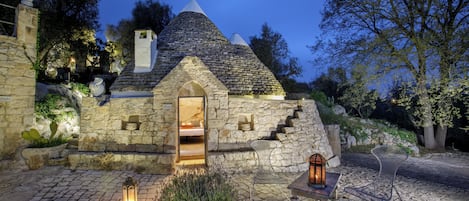 Ein Steinhaus mit einem kegelförmigen Dach und einem kleinen, gewölbten Eingang, im Inneren ist ein Bett zu sehen.