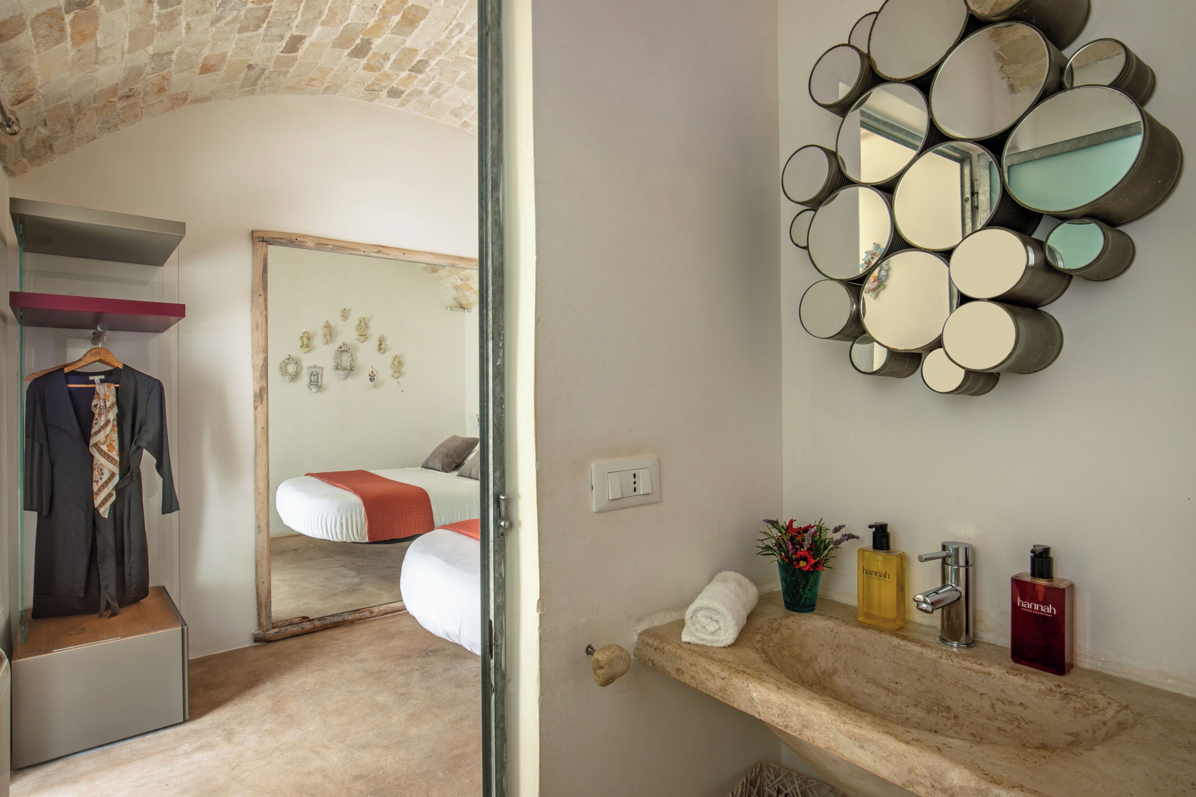 Una habitación de hotel con cama, espejo, tocador con artículos de aseo y perchero.