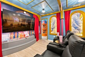 A living room with a large flat-screen TV, black leather sofa, red curtains, and a bookshelf in the background. - Orlando Most Incredible Themed 10BR Villa (Four Corners)