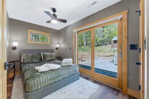 Ein Schlafzimmer mit einem Bett, einem Deckenventilator, einem großen Fenster und einer Tür zu einem Außenbereich.