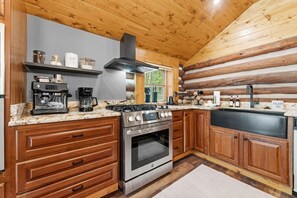 A modern kitchen with a gas stove, oven, and coffee maker. - Cozy Cabin, Sauna! Hot Tub! Filtered Lake Views! (Oakland)