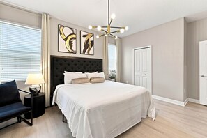 A bedroom with a large bed, a nightstand, a chair, and a ceiling light fixture. - Themed 9BR Villa, Pool, Game Room, Champions Gate (Four Corners)