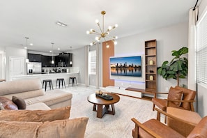 A modern living room with a sofa, coffee table, and a TV mounted on the wall. - Themed 9BR Villa, Pool, Game Room, Champions Gate (Four Corners)