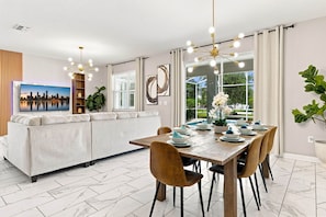 A modern dining area with a wooden table set for six, surrounded by chairs. - Themed 9BR Villa, Pool, Game Room, Champions Gate (Four Corners)