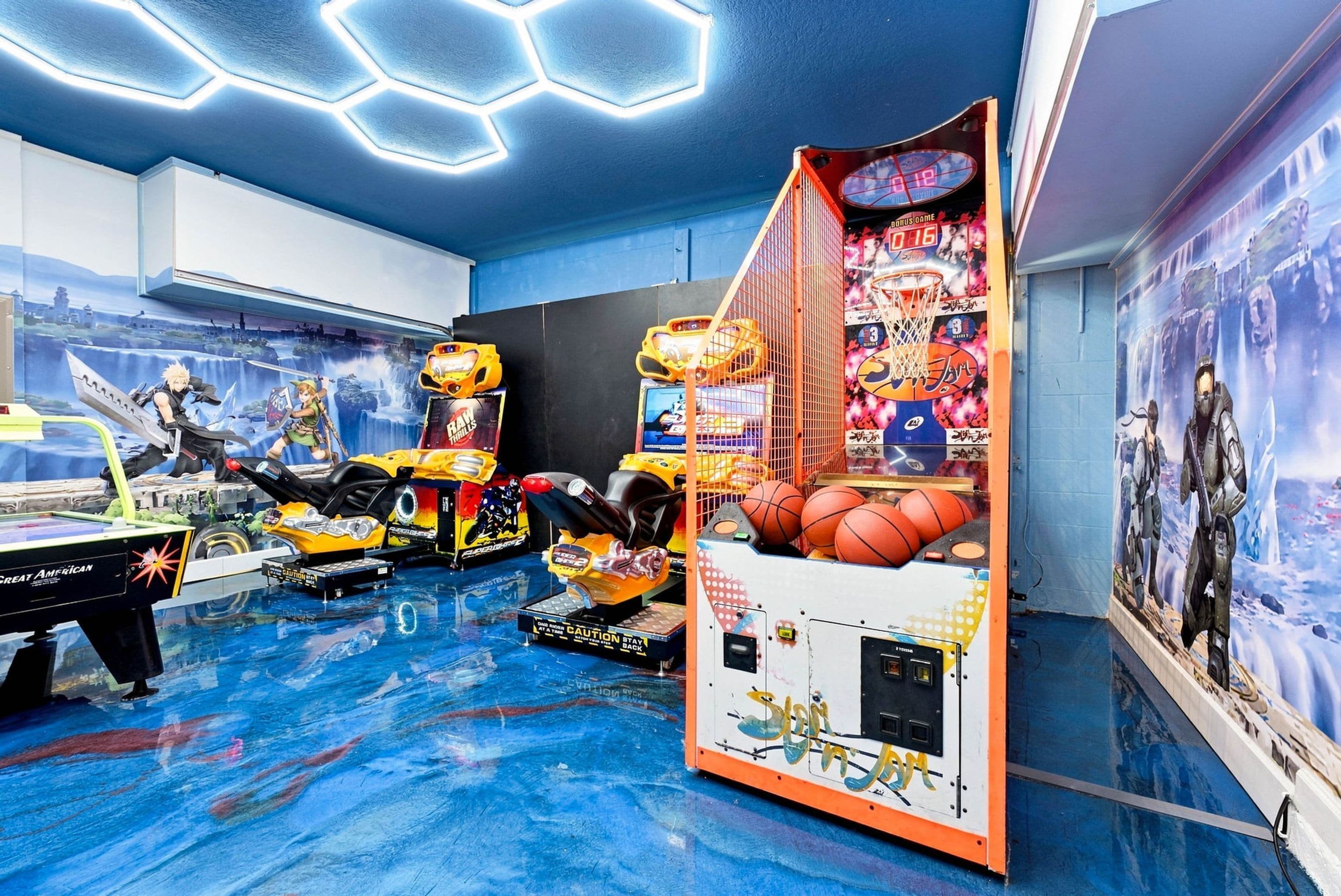 A room with a pool table, arcade games, and a basketball hoop.