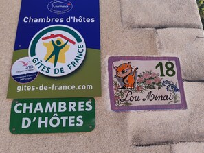 Three signs: a blue sign with 'Chambres d'hôtes' and a logo, a green sign with the same text, and a purple sign with a cat illustration and '18 Lou Minai'.