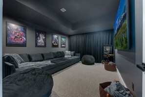 Ein modernes Wohnzimmer mit einem dunkelgrauen Sofa, einem Sitzsack, einem Fernseher und gerahmten Postern an der Wand.
