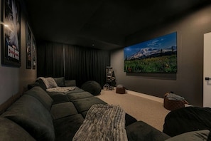 A dark-themed living room with a large flat-screen TV, a sectional sofa, and a cozy seating area. - Luxury Ski in Lodge|Indoor pool|Sleeps 21|VIEWS! (McHenry)