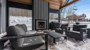 Ein überdachter Außenbereich mit Kamin, Holzmöbeln und Blick auf eine verschneite Landschaft.