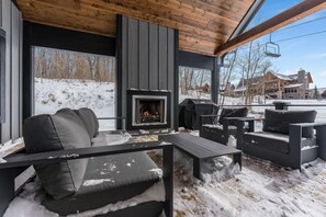 Ein überdachter Außenbereich mit Kamin, Holzmöbeln und Blick auf eine verschneite Landschaft.