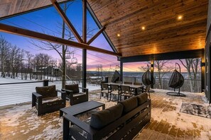 A spacious indoor area with a large window overlooking a snowy landscape, wooden ceiling, and modern seating arrangements. - Luxury Ski in Lodge|Indoor pool|Sleeps 21|VIEWS! (McHenry)