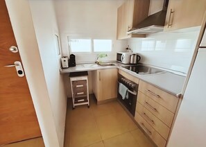 A compact kitchen with white cabinets, a microwave, a kettle, and a small oven. - Beautiful 2-Bedroom Apartment in Condado de Alhama Golf Resort with Pools, AC, WiFi (Los Guardianes)