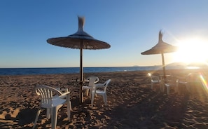 Une plage avec deux espaces aménagés avec des parasols et des chaises en plastique blanches.