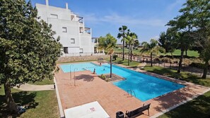 Ein Pool mit gefliestem Sonnendeck, umgeben von Bäumen und einem Gebäude im Hintergrund.