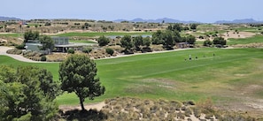 Een golfbaan met een clubhuis, een vijver en een bergachtige achtergrond.