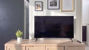 Uma sala de estar moderna com uma televisão de tela plana em um armário de madeira, uma obra de arte emoldurada na parede e um vaso de planta no armário.