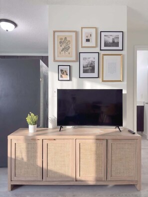 Ein modernes Wohnzimmer mit einem Flachbildfernseher auf einer Holzkommode, gerahmten Bildern an der Wand und einem Blumentopf auf der Kommode.