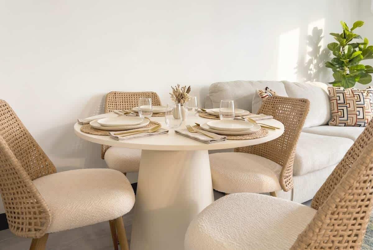 A round dining table with white chairs and a white sofa in the background.