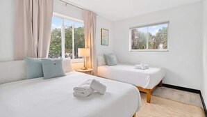 Une chambre d’hôtel avec deux lits, une fenêtre donnant sur des arbres et une lampe sur une table de chevet.