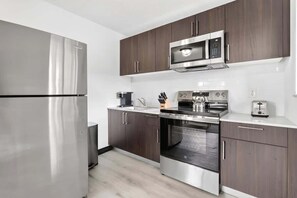 A modern kitchen with stainless steel appliances, dark wooden cabinets, and a white countertop. - Beautiful 2BR Near Beach, Airport & Las Olas (Fort Lauderdale)