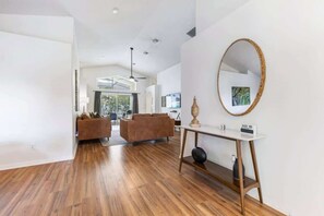 Ein modernes Wohnzimmer mit Holzboden, einem braunen Sofa, einem weißen Konsolentisch mit Spiegel und einem Deckenventilator.