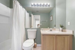 Ein Badezimmer mit Toilette, Waschbecken, Spiegel und Duschvorhang.