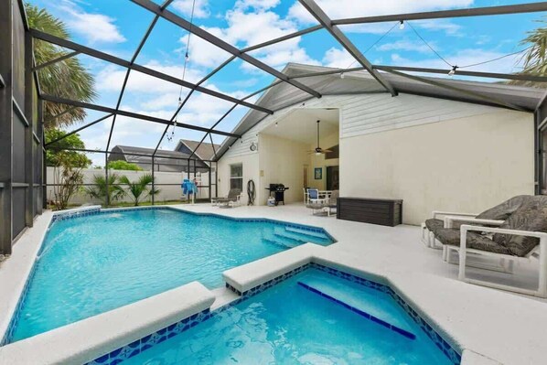 Ein Schwimmbecken mit überdachter Terrasse, Liegestühlen und Deckenventilator.