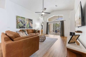 Een moderne woonkamer met een bruine leren bank, een plafondventilator en kunstwerken aan de muur.