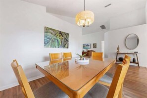Een eetruimte met een houten tafel en stoelen, een hanglamp en een schilderij aan de muur.
