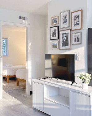 Una sala de estar moderna con un televisor de pantalla plana, un mueble blanco para entretenimiento y una cama al fondo.