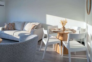 Ein modernes Wohnzimmer mit einer Couch, weißen Stühlen, einem Holzespeisetisch und einer Vase mit Trockenpflanzen.