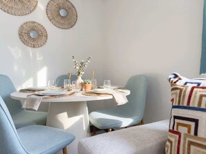 Ein Essbereich mit einem runden Tisch, hellblauen Stühlen und einer gemusterten Decke auf einem Sofa.