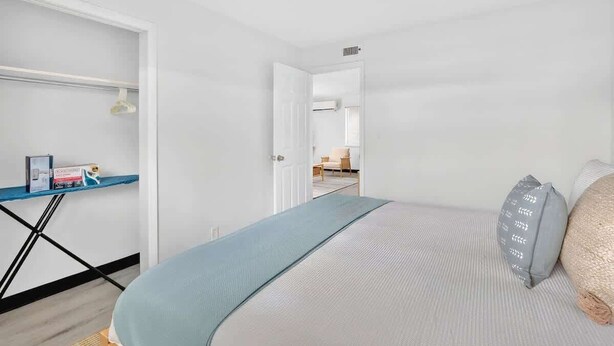 A hotel room with a bed, a desk with a chair, and a view of another room through an open door. - Cozy 2BR Near Beach, Airport & Las Olas (Fort Lauderdale)