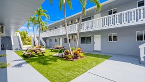 A hotel with a covered outdoor area, palm trees, a picnic table, and a well-maintained lawn. - Cozy 2BR Near Beach, Airport & Las Olas (Fort Lauderdale)