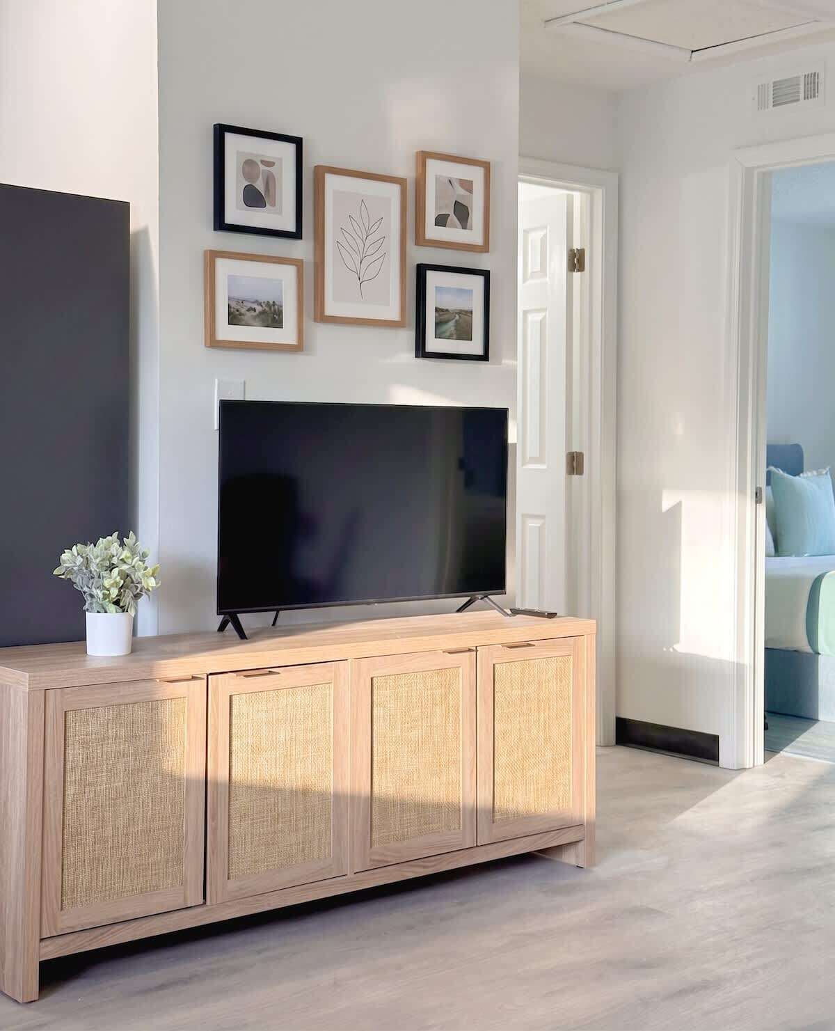 Een moderne woonkamer met een grote flatscreen televisie, een licht houten kast en lijstwerken aan de muur.