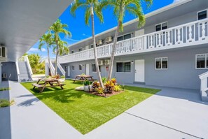 A modern building with a covered outdoor area, a staircase, and a well-maintained lawn with palm trees. - Newly Renovated 2BR Near Beach, Airport & Las Olas (Fort Lauderdale)