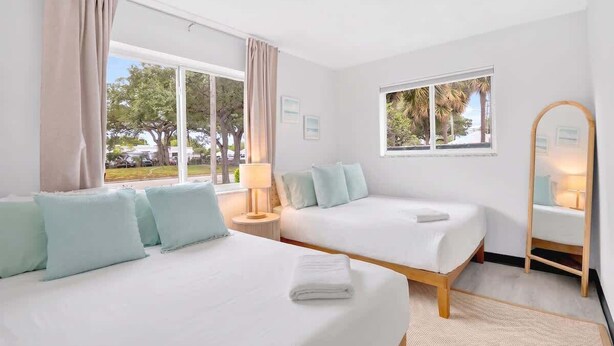 A hotel room with two beds, a window with a view of trees, a mirror, and a lamp. - Inviting 2BR Near Beach, Airport & Las Olas (Fort Lauderdale)