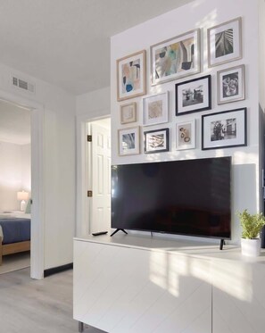 Ein modernes Wohnzimmer mit einem großen Flachbildfernseher, der an einem weißen Schrank befestigt ist, umgeben von gerahmten Bildern an der Wand.