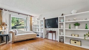 Een kamer met een bank, houten vloer, een televisie en planken met diverse spullen.