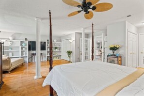 A spacious bedroom with a large bed, a ceiling fan, and a view into the adjacent living area.