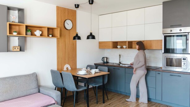 A modern kitchen with a dining area, a clock, and a person preparing food. - Little Rome Loft - Vibe Apartment (Trnava)