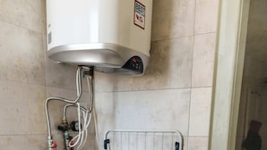 A compact laundry area with a washing machine and dryer, a water heater, and a metal rack. - Little Rome Loft - Vibe Apartment (Trnava)
