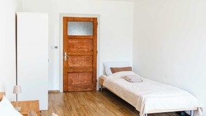 A room with a wooden door, a bed with a white bedspread, and a bedside table. - Little Rome Loft - Vibe Apartment (Trnava)