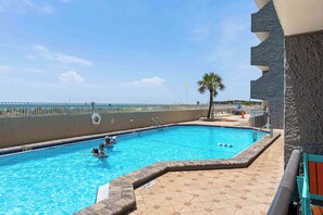Une piscine avec une terrasse carrelée, un poste de surveillance pour les sauveteurs et un palmier.