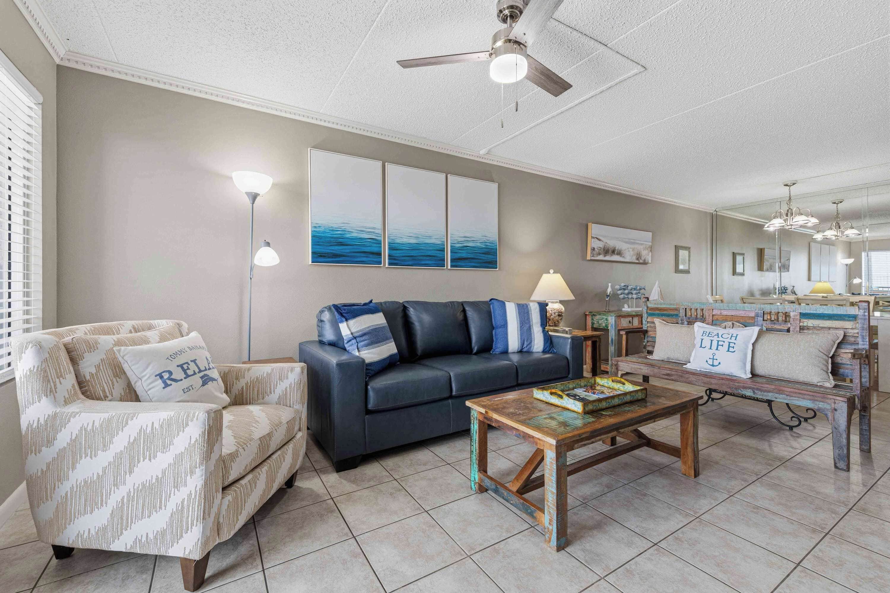 A living room with a sofa, armchair, coffee table, and artwork on the wall.