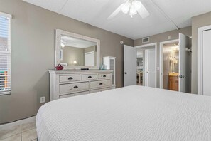 A bedroom with a large bed, a dresser with drawers, a mirror, and a ceiling fan. - Waterfront Condo with shared pool & fitness room (Fort Walton Beach)