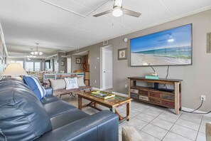 Un salon avec un canapé en cuir, une table basse, un téléviseur et un tableau sur le thème de la plage.