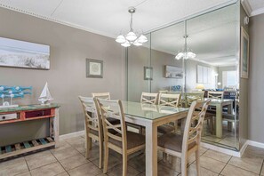 A dining area with a glass table, wooden chairs, a chandelier, and a large mirror reflecting the room. - Waterfront Condo with shared pool & fitness room (Fort Walton Beach)
